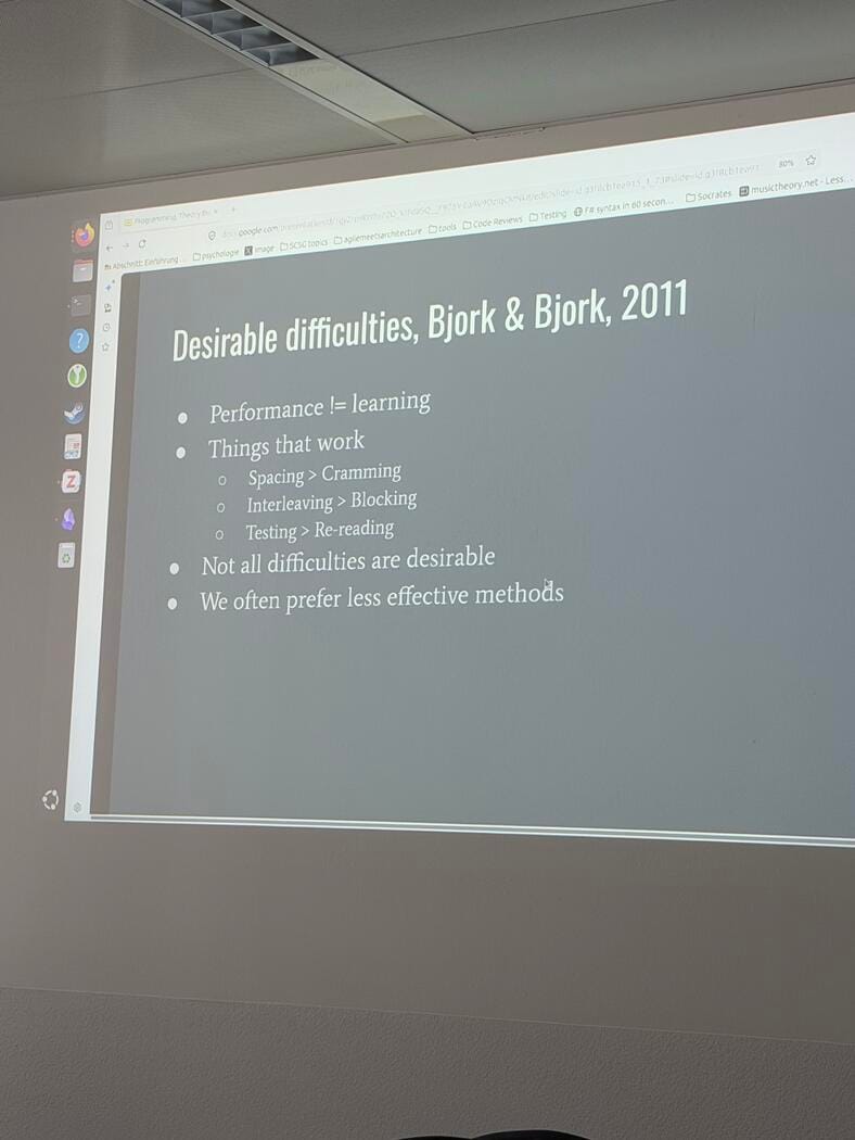 A projector screen shows a slide titled Desirable difficulties, Bjork and Bjork, 2011, listing that performance is not learning, spacing over cramming, interleaving over blocking, testing over re-reading, that not all difficulties are desirable, and that we often prefer less effective methods.